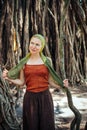 Beautiful slender woman on the background of natural wood. Cheerful young girl with scarf on her head posing against the Banyan