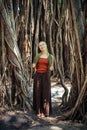 Beautiful slender woman on the background of natural wood. Cheerful young girl with scarf on her head posing against the Banyan