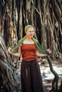 Beautiful slender woman on the background of natural wood. Cheerful young girl with scarf on her head posing against the Banyan