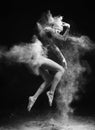 Beautiful slim girl wearing a gymnastic bodysuit covered with clouds of the flying white powder jumps dancing on a dark. Artistic Royalty Free Stock Photo