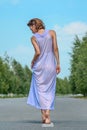 Beautiful slim model girl in a purple silk dress from the back on the road Royalty Free Stock Photo