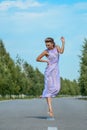 Beautiful slim model girl in a purple silk dress gently posing in dancing jump on the road