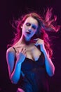 Beautiful slim busty blonde girl wearing black bodysuit lit up in pink and blue light smiles and sensually touches her neck