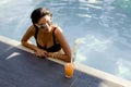 Beautiful slim woman in bikini and sunglasses relaxing and drink cocktail on poolside of a swimming pool Royalty Free Stock Photo