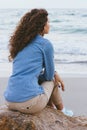 Beautiful slim woman with curly hair sitting on a rock