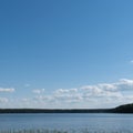 A beautiful small forest lake combined with a wide swath of summer blue skies with fluffy clouds. Royalty Free Stock Photo