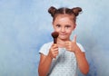 Beautiful small kid girl applying tonal cosmetic brush and showing thumb up sign on blue background with empty copy space