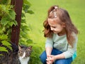 Beautiful small kid girl looking and playing with cat on green grass summer sunny bright background. Closeup Royalty Free Stock Photo