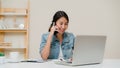 Beautiful smart business Asian woman in smart casual wear working on laptop and talking on phone while sitting on table in Royalty Free Stock Photo