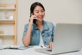 Beautiful smart business Asian woman in smart casual wear working on laptop and talking on phone while sitting on table in Royalty Free Stock Photo