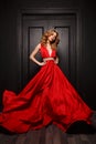 Beautiful smart dressed woman in the red evening fluttering dress is posing, the wooden door is on the background