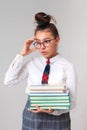 A beautiful and smart girl loves to study. A schoolgirl with glasses and a tie holds a stack of books and looks thoughtfully