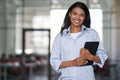 Portrait of a young cheerful beautiful business woman holding digital tablet, looking at camera and smiling while Royalty Free Stock Photo