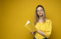 Beautiful smart young girl holding and reading book isolated on the yellow background. Portrait of attractive woman in a Royalty Free Stock Photo