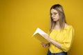 Beautiful smart young girl holding and reading book isolated on the yellow background. Portrait of attractive woman in a Royalty Free Stock Photo