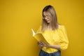 Beautiful smart young girl holding and reading book isolated on the yellow background. Portrait of attractive woman in a Royalty Free Stock Photo