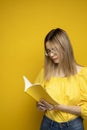 Beautiful smart young girl holding and reading book isolated on the yellow background. Portrait of attractive woman in a Royalty Free Stock Photo