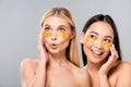 Smiling asian and surprised european naked girls with eye patches isolated on grey