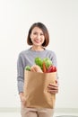 Beautiful smiling Asian woman holding paper shopping bag full of vegetables and groceries, studio shot isolated on white Royalty Free Stock Photo