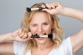 Beautiful smiling blond woman with curly hair, clean skin and fresh make-up holds makeup brushes in her hands. Aesthetic