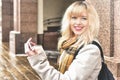 Beautiful smiling blonde caucasian girl walking in the city and straightening her makeup looking in the makeup mirror Royalty Free Stock Photo