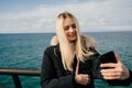 A beautiful smiling blonde girl makes a selfie on the phone against the background of the sea. Royalty Free Stock Photo