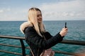 A beautiful smiling blonde girl makes a selfie on the phone against the background of the sea. Royalty Free Stock Photo