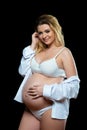 Beautiful smiling blonde pregnant woman in white clothes on a black background. Women`s health and happy pregnancy Royalty Free Stock Photo