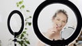 Beautiful smiling blonde woman with blue eyes puts her lipstick in front of the mirror and a ring light lamps, concept of makeup Royalty Free Stock Photo