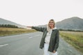 Beautiful smiling blonde young woman traveler in white hoodie on road, trip to mountains, hitching a ride Royalty Free Stock Photo