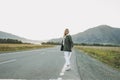 Beautiful smiling blonde young woman traveler in white hoodie on road, trip to mountains, hitching a ride Royalty Free Stock Photo