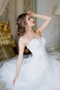 A beautiful smiling bride with chic makeup and hairstyle in a white wedding dress sits on a bed Royalty Free Stock Photo