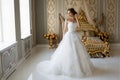 A beautiful smiling bride with chic makeup and hairstyle in a white wedding dress is standing in a bedroom Royalty Free Stock Photo