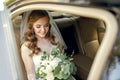 A beautiful smiling bride on her wedding day sits in the car and holds a wedding bouquet of white roses Royalty Free Stock Photo