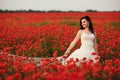 Beautiful smiling bride walking through red poppy fild at sunset