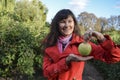 Beautiful smiling brunette girl in red coat holding fresh green apple on palm of her hand over nature background Royalty Free Stock Photo