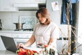 Beautiful smiling brunette young woman plus size body positive using laptop in kitchen at the home