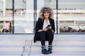 Beautiful smiling business woman using mobile phone sitting on stairs in city. Buildings background Royalty Free Stock Photo