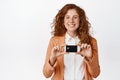 Beautiful smiling businesswoman showing credit card, wearing suit, standing over white background Royalty Free Stock Photo