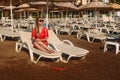 Beautiful smiling Caucasian woman in a red transparent tunic and sunglasses lying on a white sunbed on the beach in a hotel