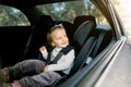 Beautiful smiling cute baby girl fastened with security belt in safety car seat, looking at the window. Child Royalty Free Stock Photo