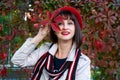 beautiful smiling elegant woman in red beret and with bright red lipstick on her lips holds an autumn leaf in her hand. Royalty Free Stock Photo