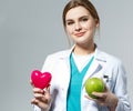 Beautiful smiling female doctor holding red heart and green apple Royalty Free Stock Photo