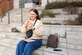 Beautiful smiling female student using smartphone outdoors. Happy cheerful young woman sitting on stairs on city street Royalty Free Stock Photo