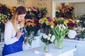 A beautiful smiling florist creates a composition of white flowers in a flower shop.