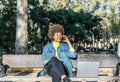 Beautiful smiling girl with afro hair speaks on her mobile phone sitting on the bench of a large park Royalty Free Stock Photo