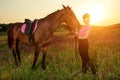 Beautiful smiling girl jockey stand next to her brown horse wearing special uniform on a sky and green field background Royalty Free Stock Photo