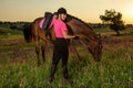 Beautiful smiling girl jockey stand next to her brown horse wearing special uniform on a sky and green field background Royalty Free Stock Photo