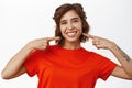 Beautiful smiling girl pointing fingers at her white teeth, looking happy, standing in tshirt over white background Royalty Free Stock Photo