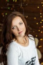 Beautiful smiling girl in warm white jacket sits near the window next to the wall in the lights Royalty Free Stock Photo